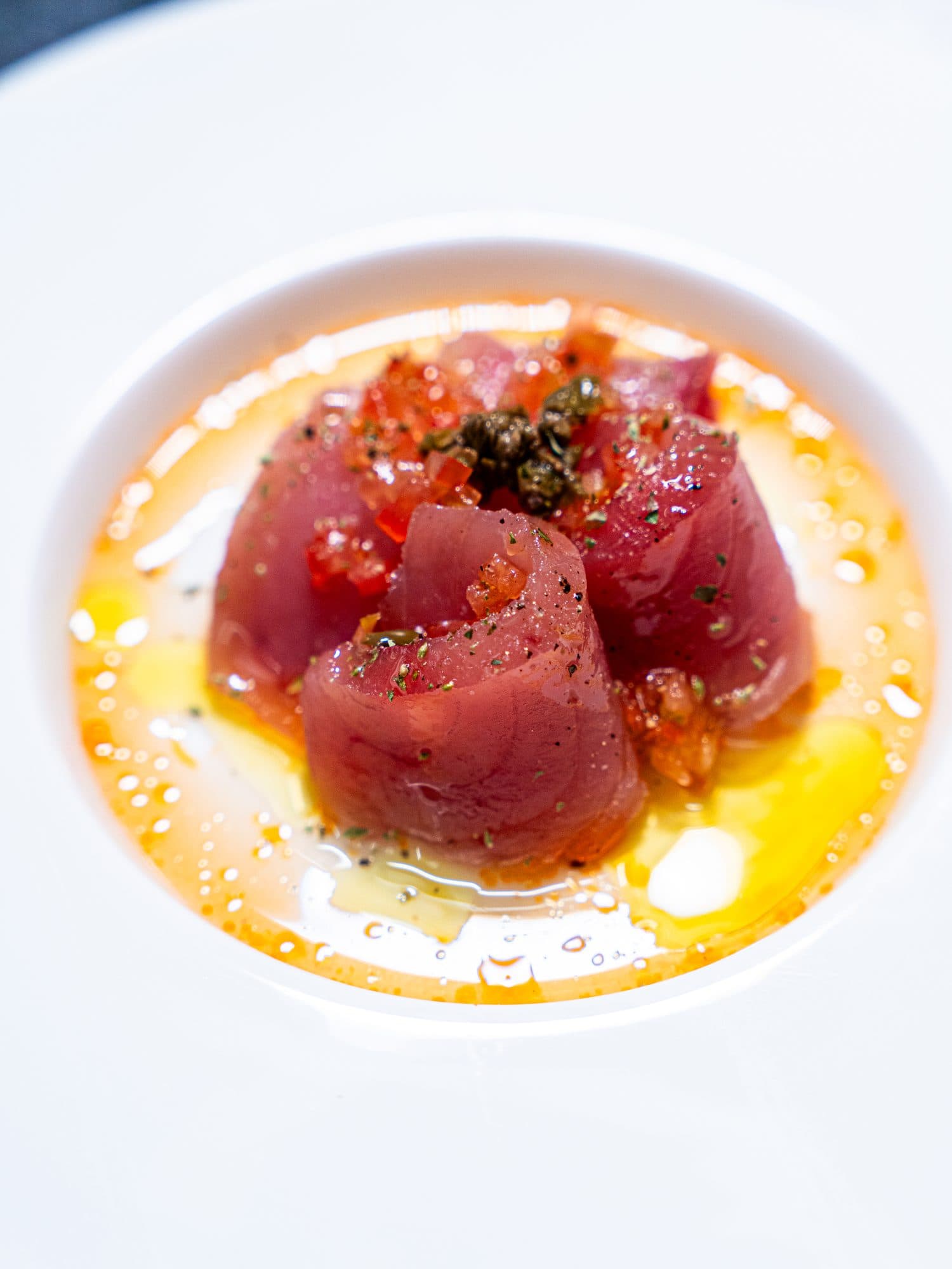 Tranci di tonno crudo arrotolati, in un fondo arancione con olio e pomodoro.