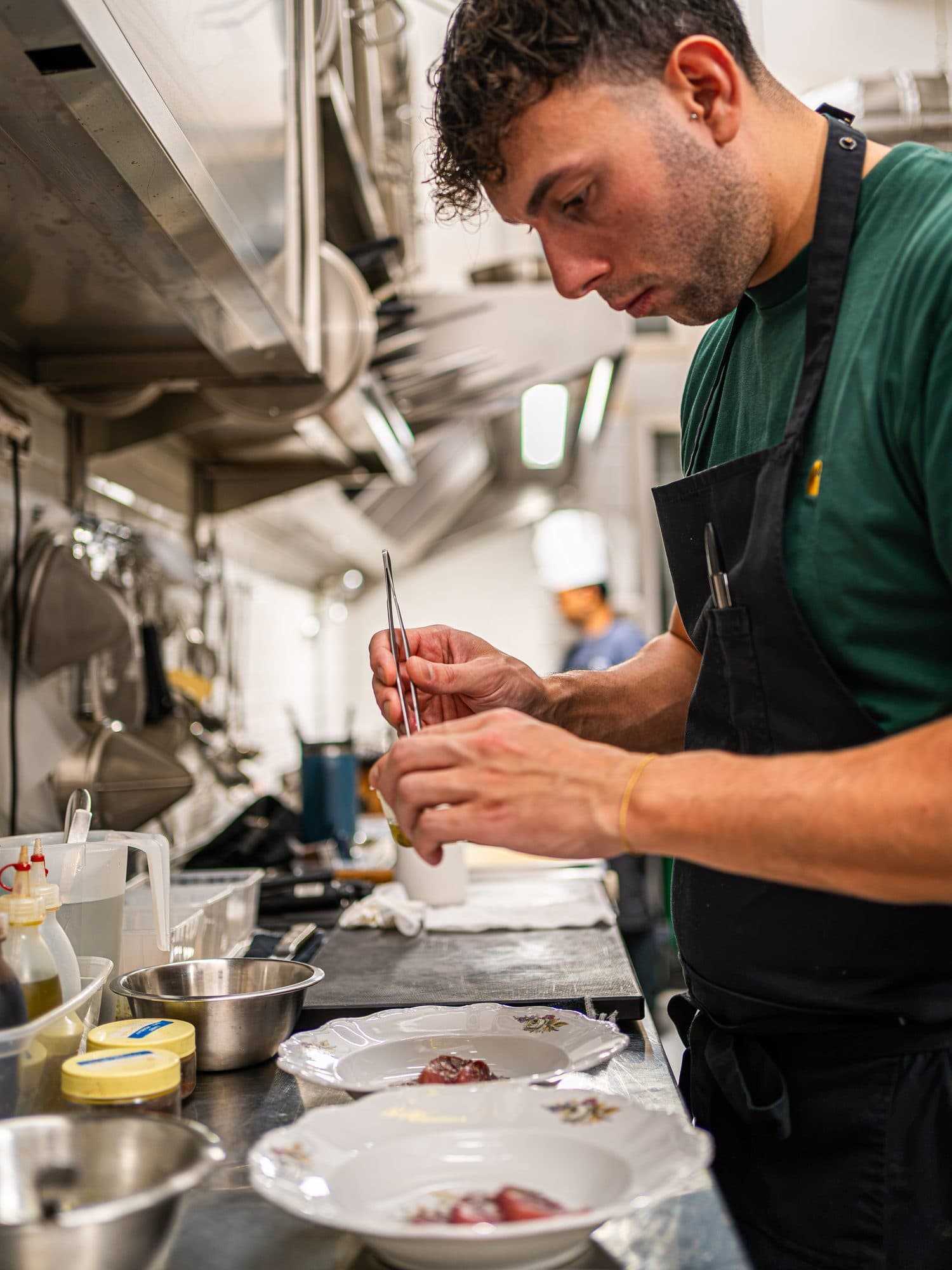 Pierpaolo Presta in cucina, con la pinzetta, mentre finisce due piatti di pesce crudo.