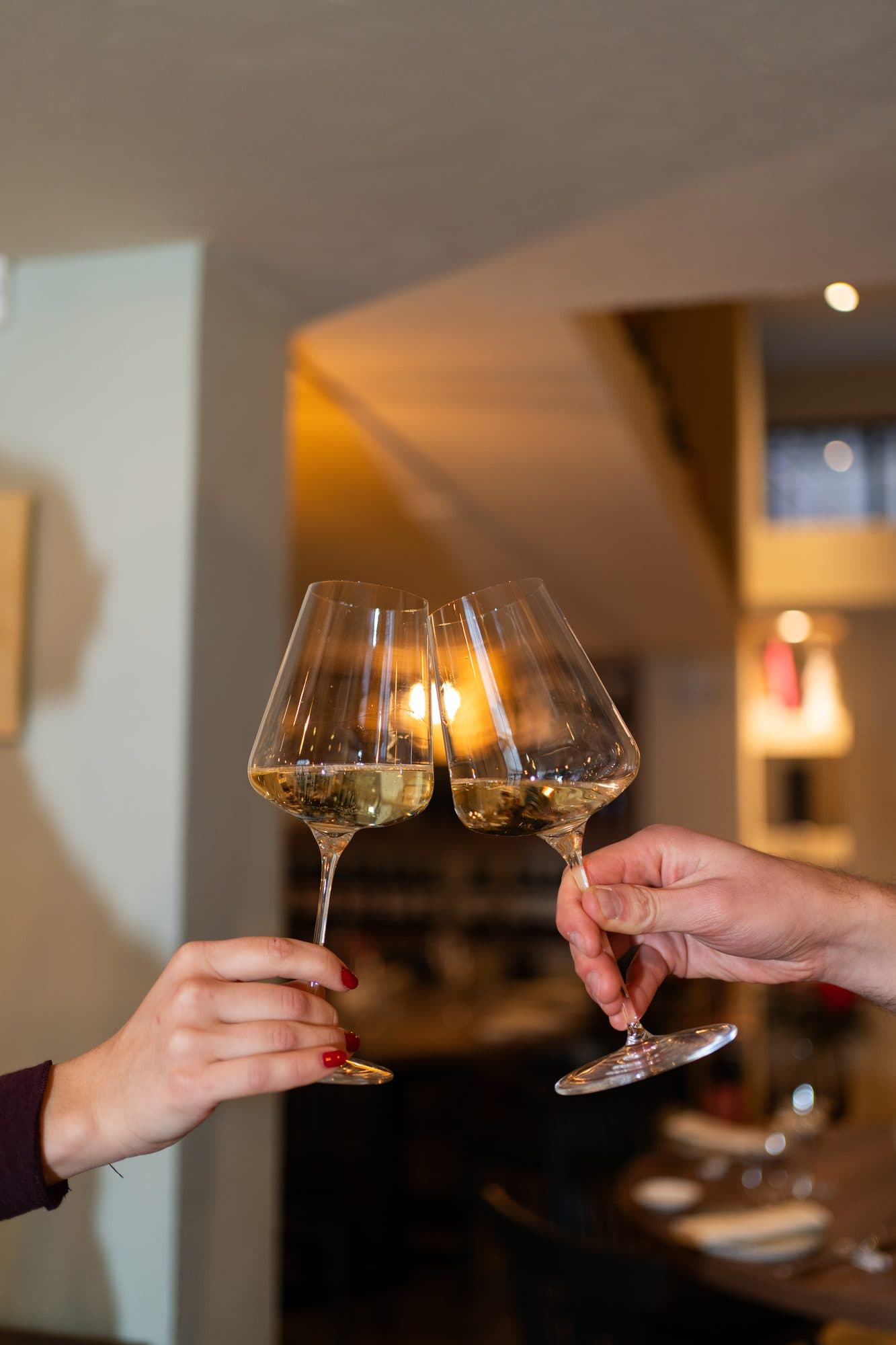Due calici di vino bianco che brindano, nella sala del ristorante.